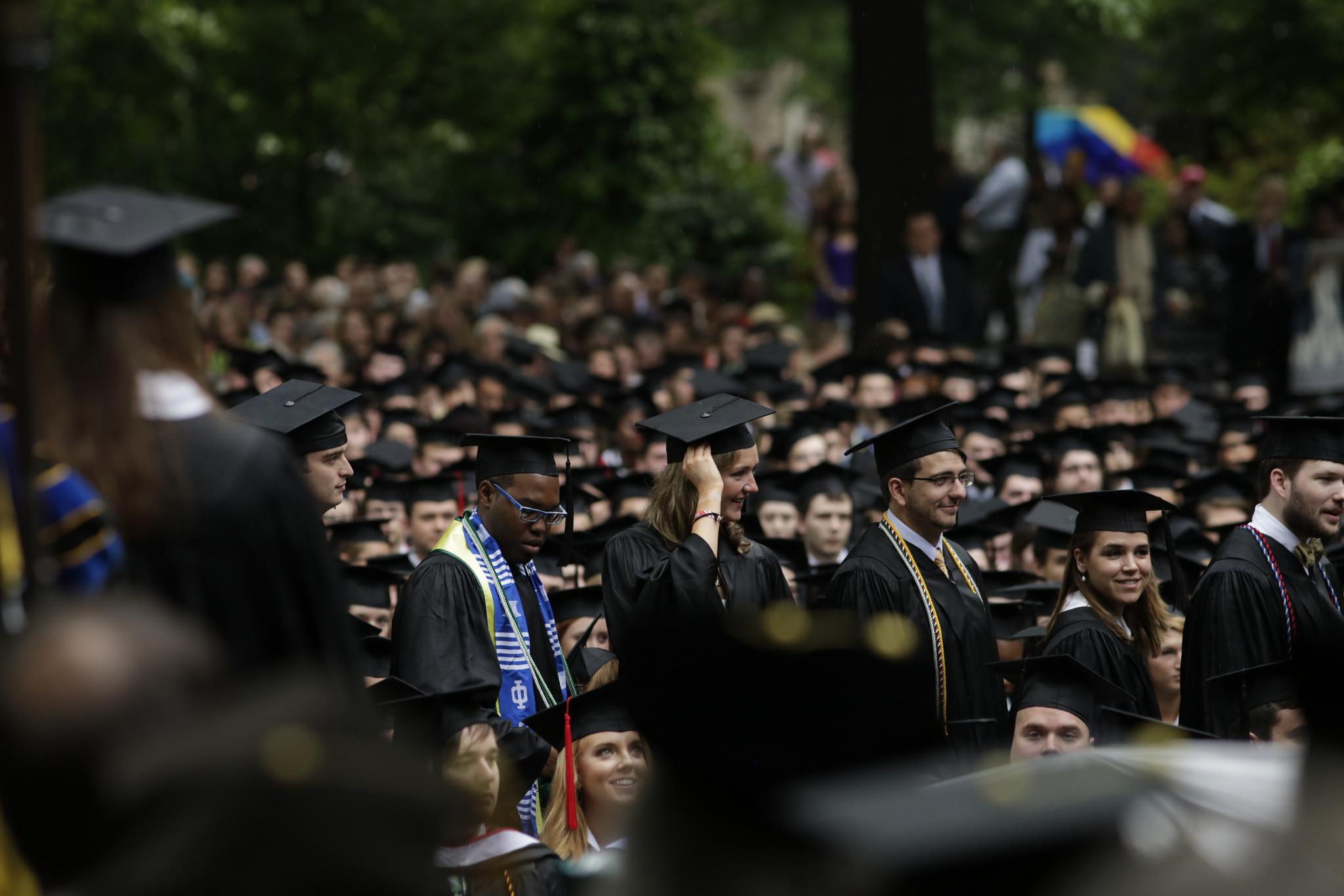 一群头戴帽子、身穿长袍的毕业生从一排排坐着的毕业生中间走过