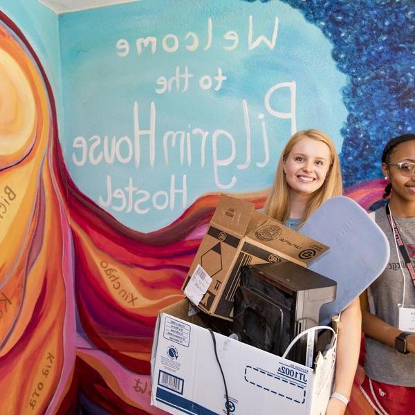 两名女学生在一幅壁画前提着盒子